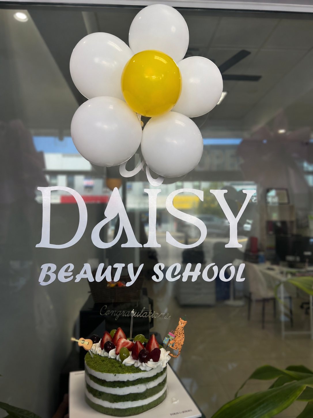 Daisy Beauty School front window with a celebratory cake and daisy balloons